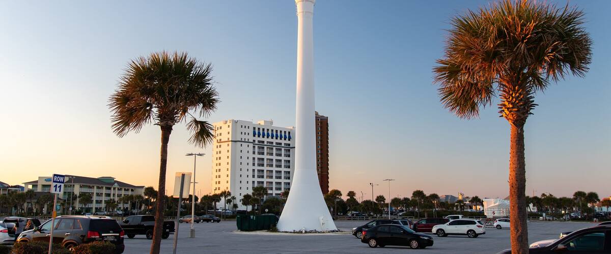 Ein großer Wasserturm mit Strandmotiv, Palmen und einem Parkplatz mit Autos.