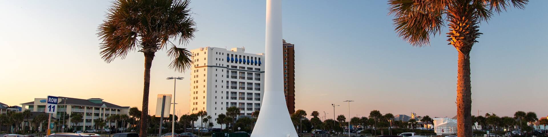 A large water tower with a beach-themed design, palm trees, and a parking lot with cars.