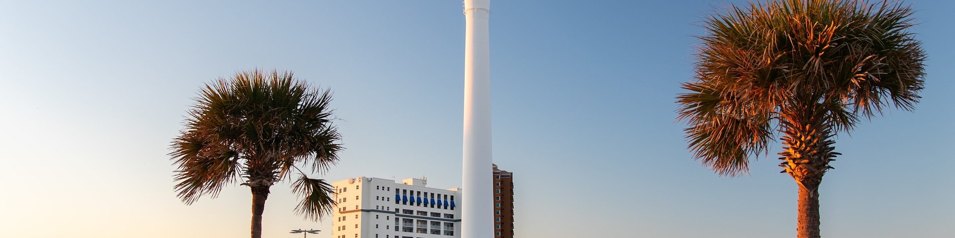 Uma grande torre de água com design praiano, palmeiras e um estacionamento com carros.