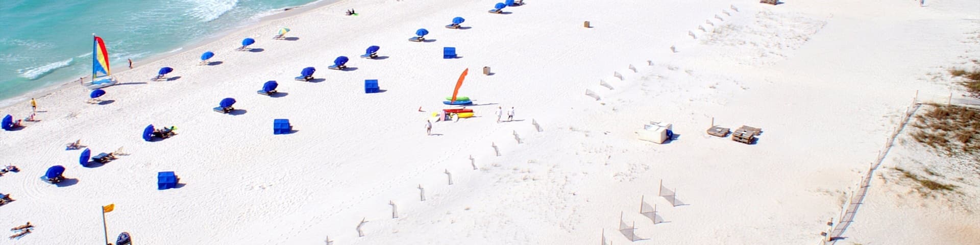 A beach with rows of blue umbrellas and a pier extending into the ocean.