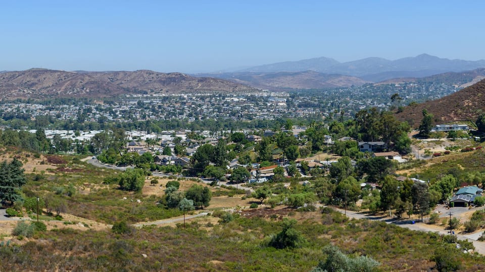 A valley with a town nestled between hills, a winding road, and distant mountains.