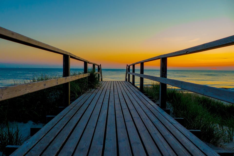 A wooden boardwalk leading to the ocean at sunset.