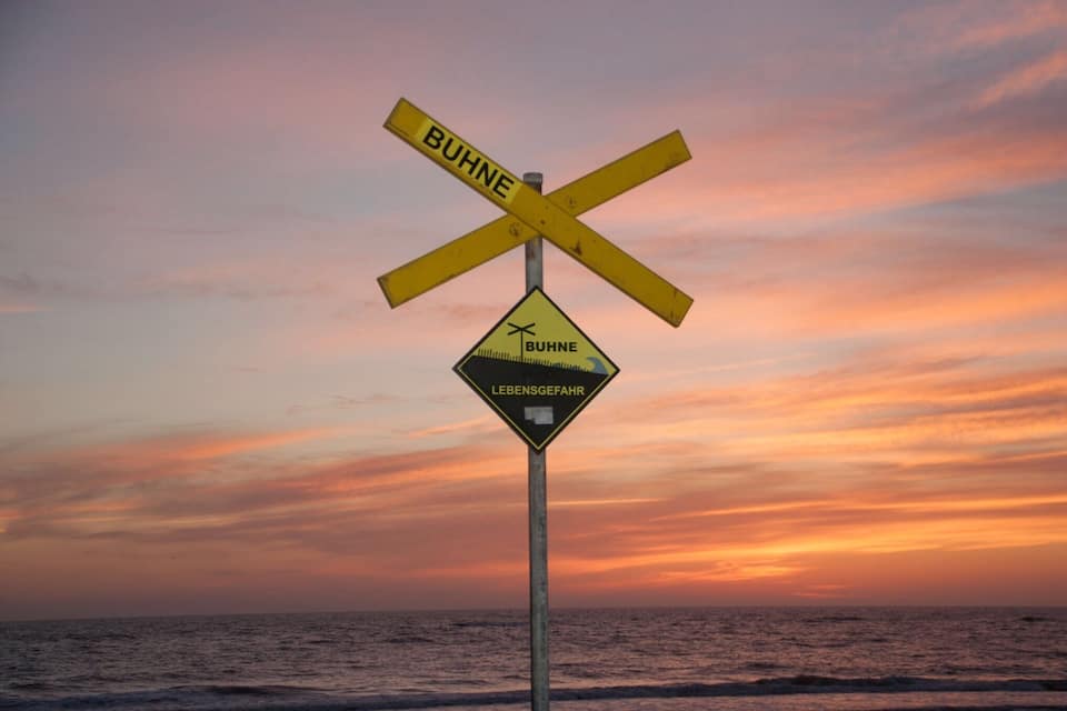 A railway crossing sign with 'BUHNE' and 'LEBENSGEFAHR' written on it, set against a sunset sky.