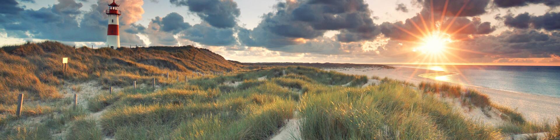 A lighthouse on a grassy hill, a beach, and a sunset over the ocean.