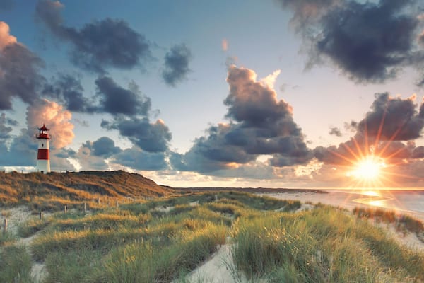Ein Leuchtturm auf einer grasbewachsenen Anhöhe, ein Strand und ein Sonnenuntergang über dem Ozean.