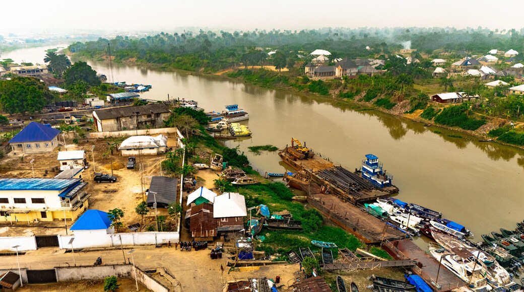 Aerial view of a waterway reflecting the sky, with boats docked along the banks near buildings and lush greenery, Yenagoa, Bayelsa Stae, Nigeria.