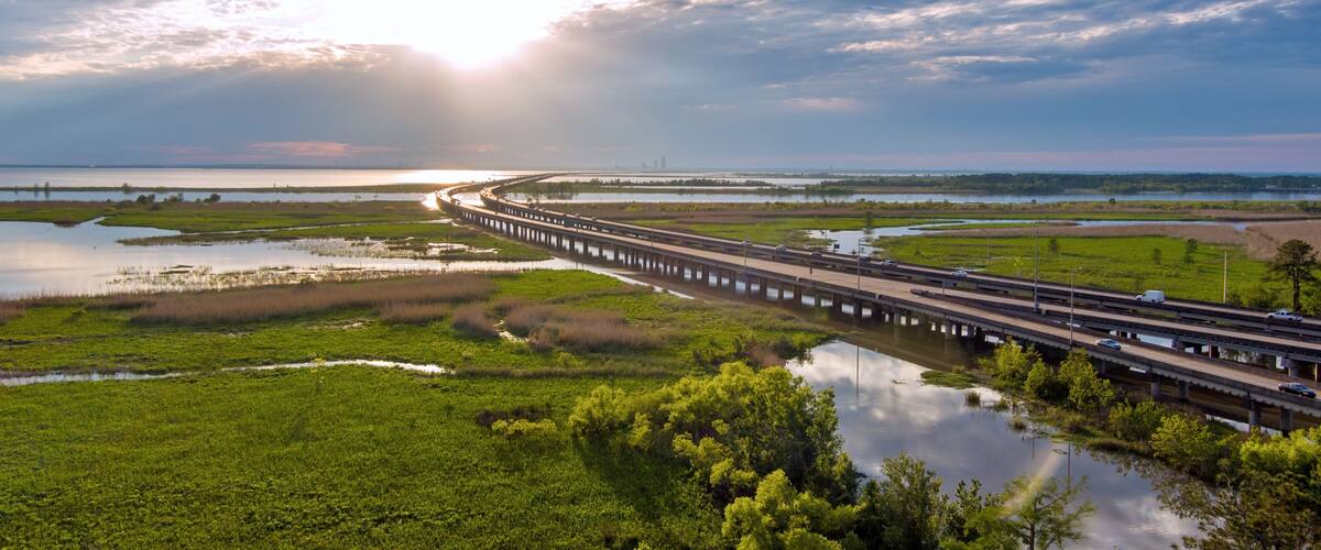 A bridge over a marshy landscape with a sunset in the background.