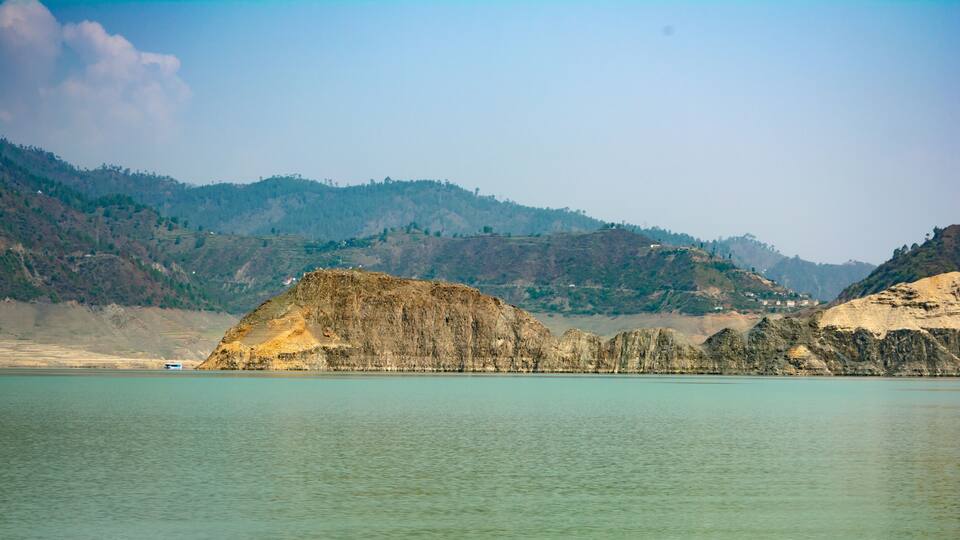 A calm lake with a rocky outcrop in the foreground and hills in the background.