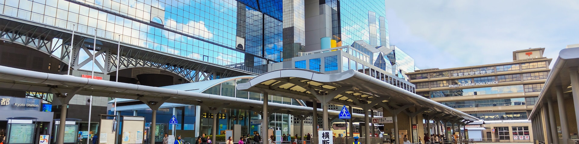 Une gare moderne dotée d’une façade en verre et d’une passerelle piétonne couverte.