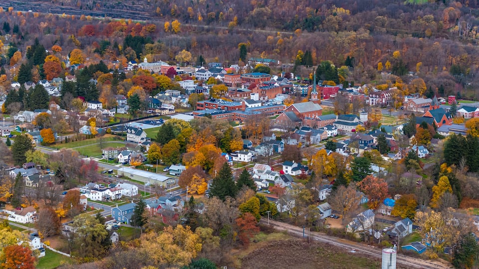 An aerial view of a town with autumn-colored trees, a mix of residential and commercial buildings, and a railway track.