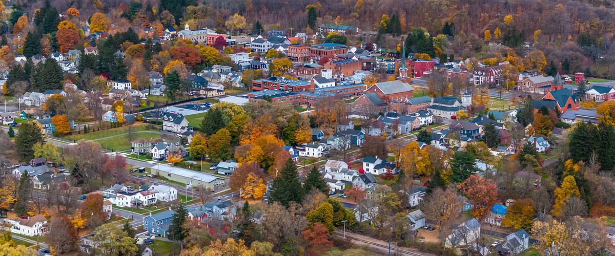 An aerial view of a town with autumn-colored trees, a mix of residential and commercial buildings, and a railway track.