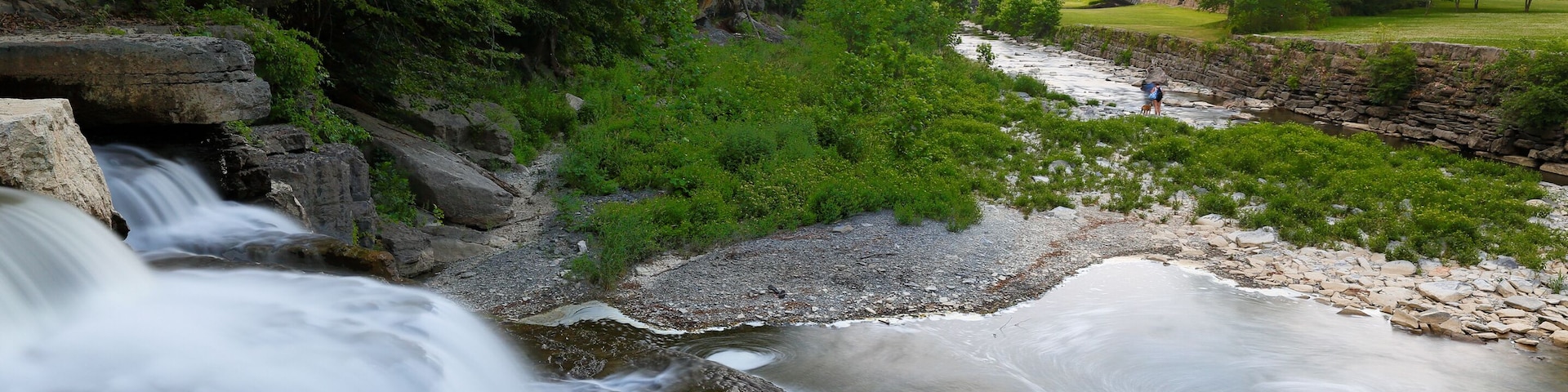 Un río serpentea por una zona boscosa con un puente de piedra al fondo.