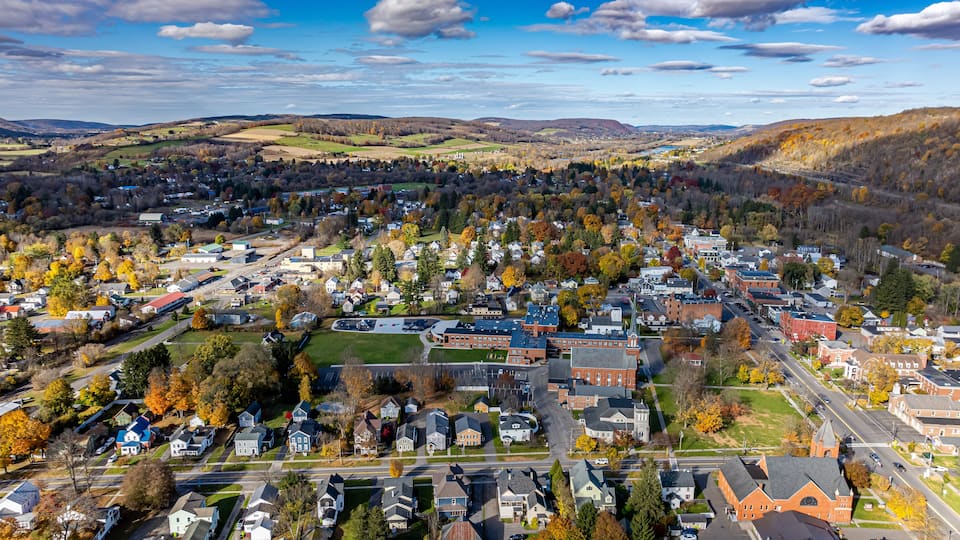 A town with autumn-colored trees, a central church, and rolling hills in the background.