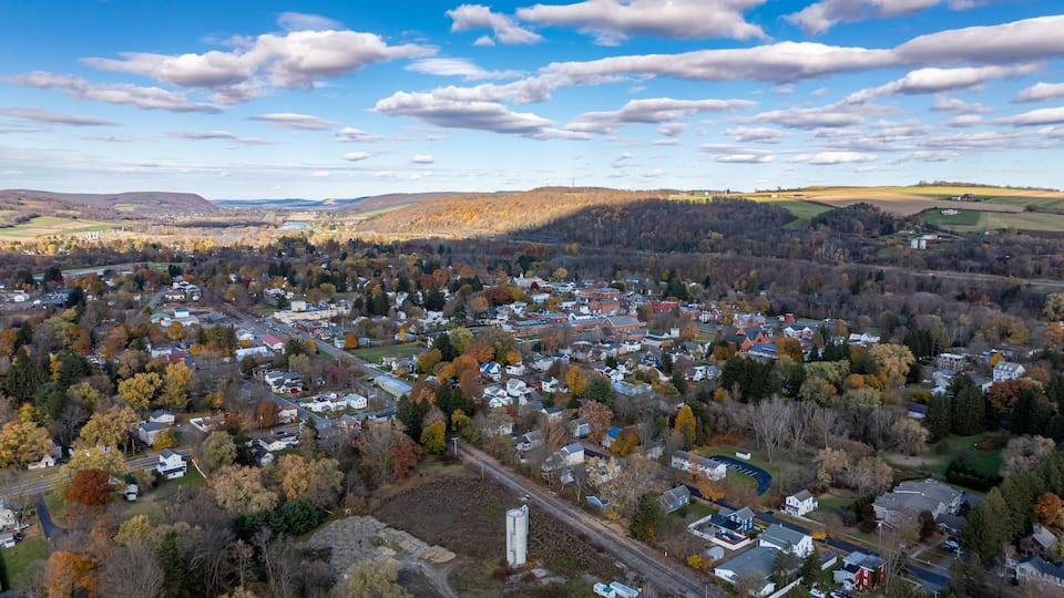 A town with autumn-colored trees, a river, and rolling hills in the background.