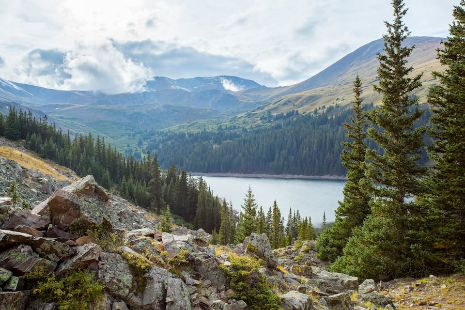 A mountainous landscape with a lake, dense forests, and rocky terrain.