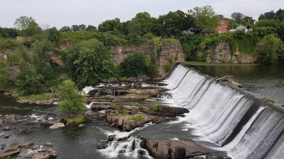 A dam with multiple waterfalls, surrounded by lush greenery and rocky cliffs.