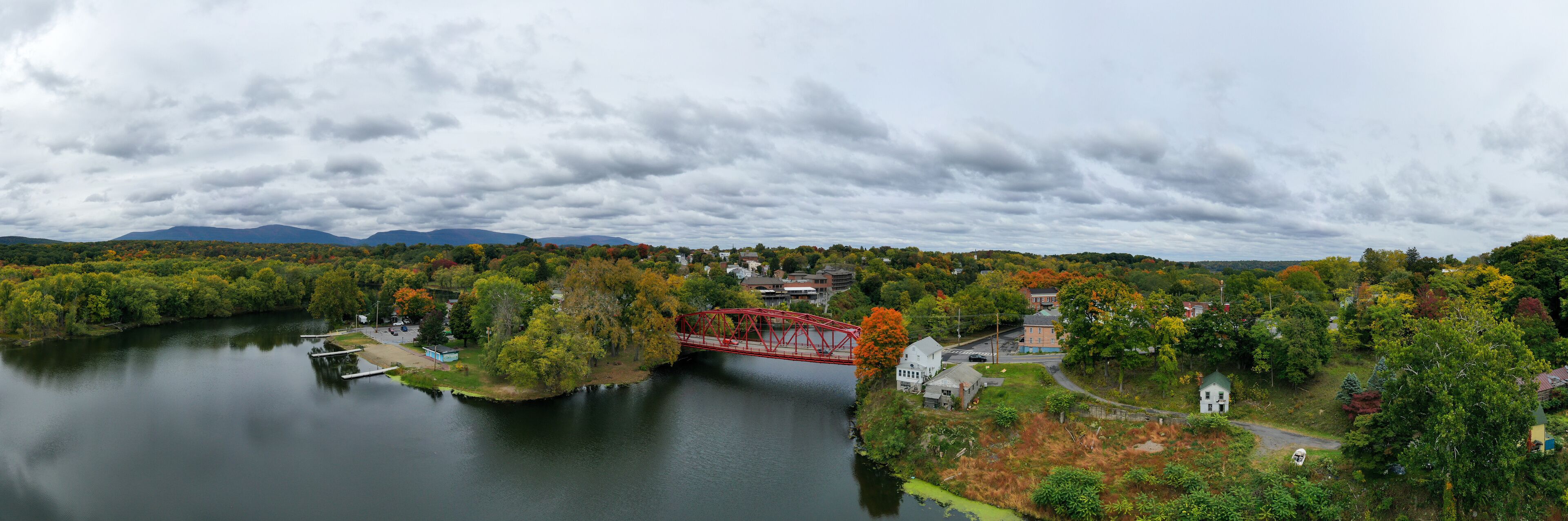 A river with a red bridge, surrounded by autumn-colored trees and houses.