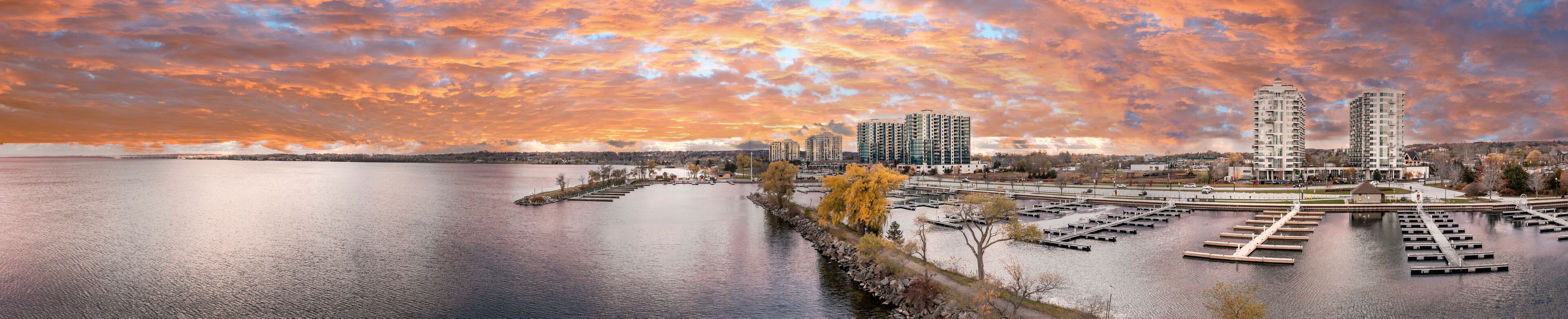 A waterfront marina with boats, a dock, and high-rise buildings under a colorful sunset sky.