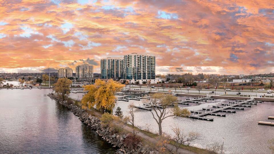 A waterfront marina with boats, a dock, and high-rise buildings under a colorful sunset sky.