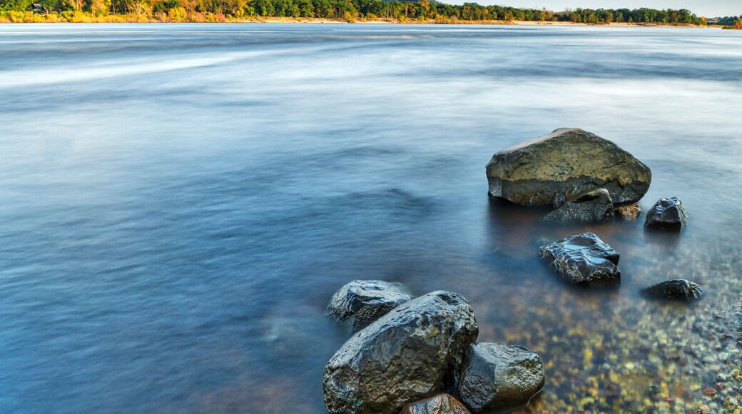 A river with smooth water surface, surrounded by rocks and a forested hillside.
