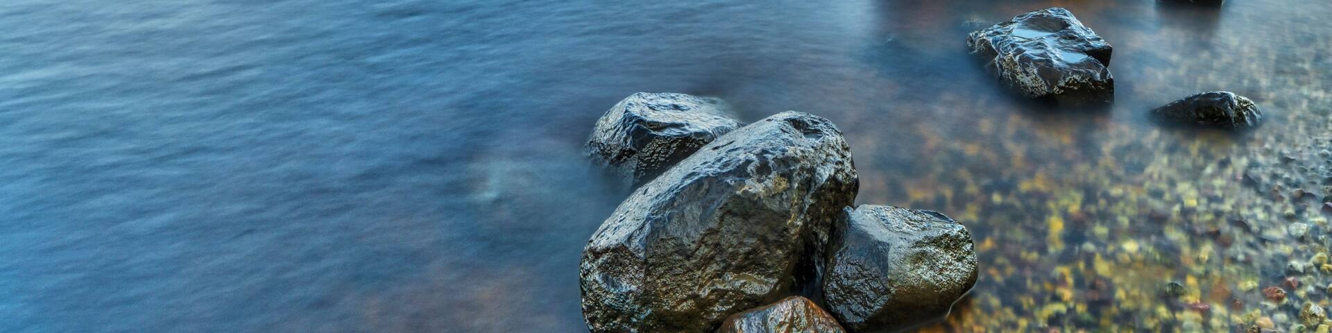 A river with smooth water surface, surrounded by rocks and a forested hillside.
