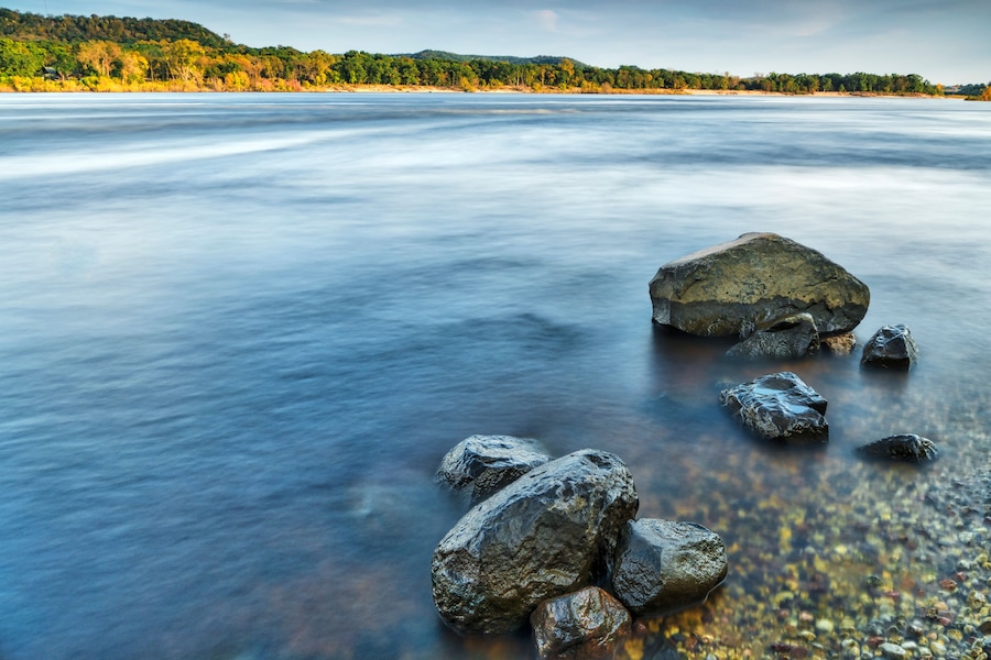 A river with smooth water surface, surrounded by rocks and a forested hillside.