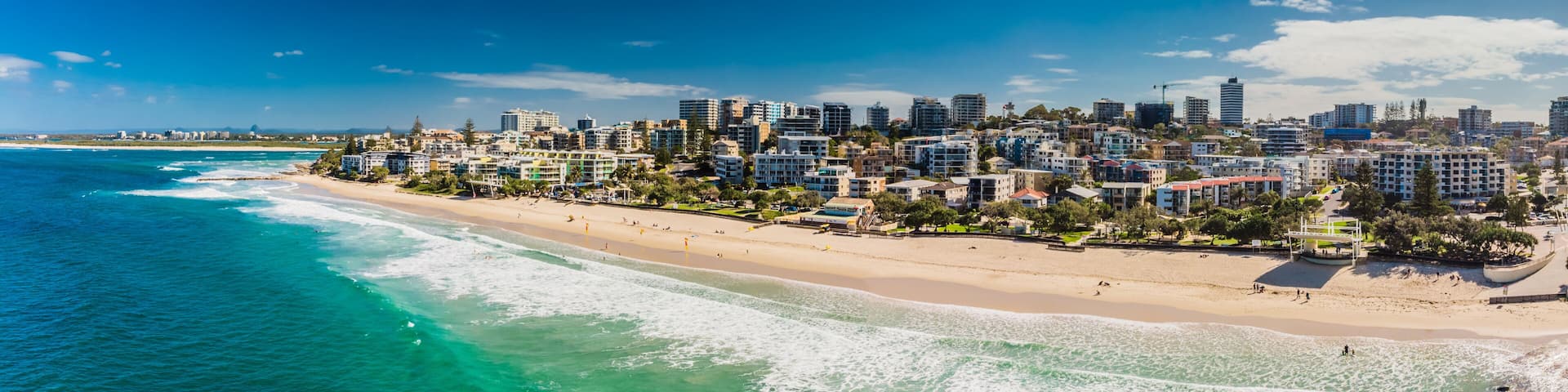 A coastal cityscape with a beach, buildings, and clear blue waters.