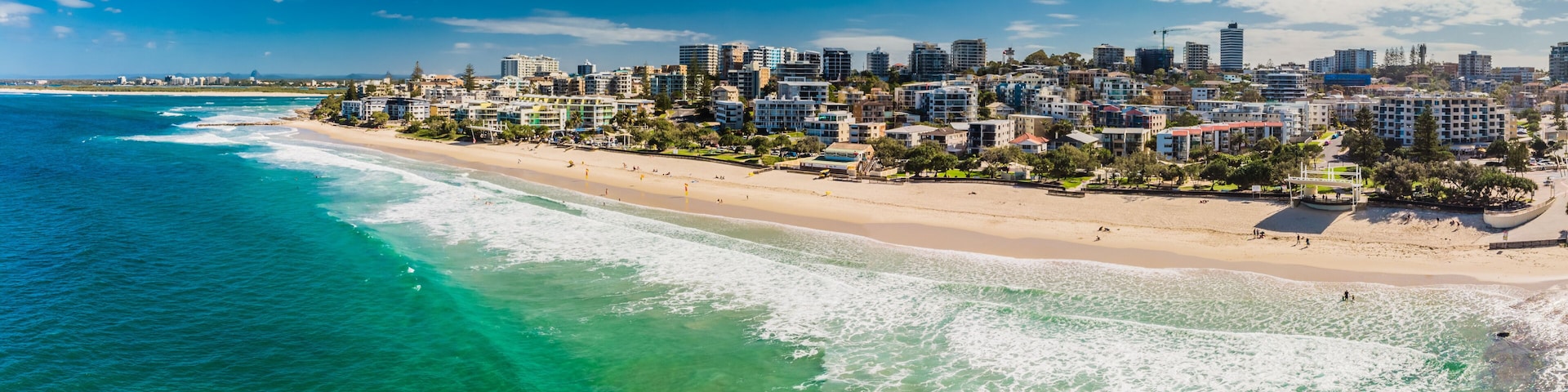 Paisagem costeira com praia, edifícios e águas azul-claras.