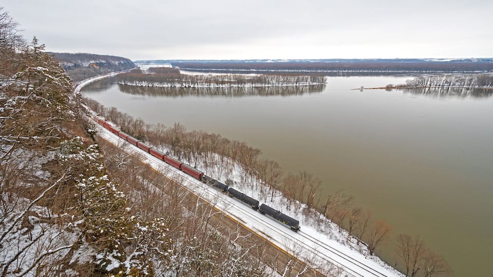 A train traveling along a snowy railway track beside a large body of water.
