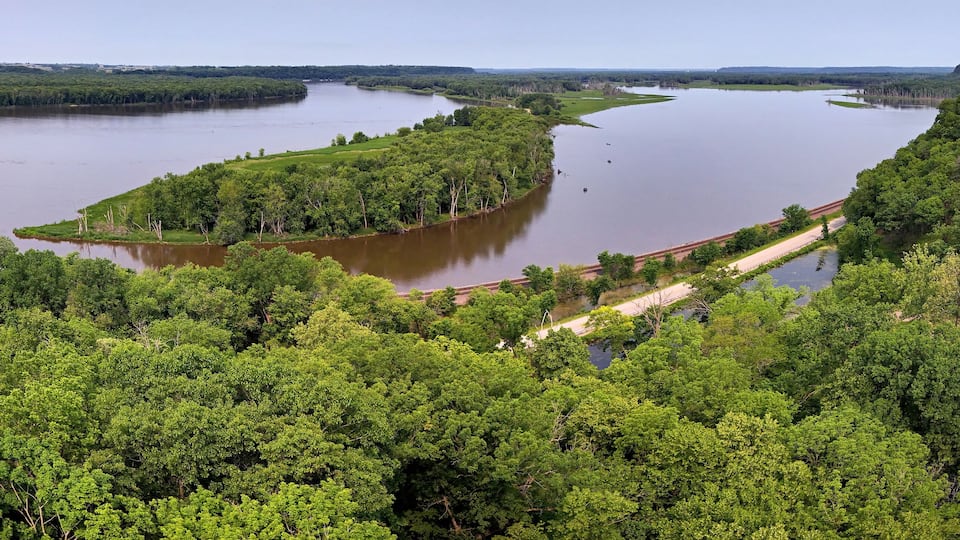 A river winding through a densely forested landscape with a railway track running alongside it.