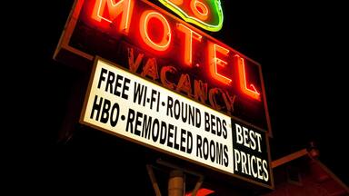 Un letrero de motel con neón que anuncia 'INTERNET GRATIS - CAMAS REDONDAS' y 'HABITACIONES REMODELADAS - HBO'.