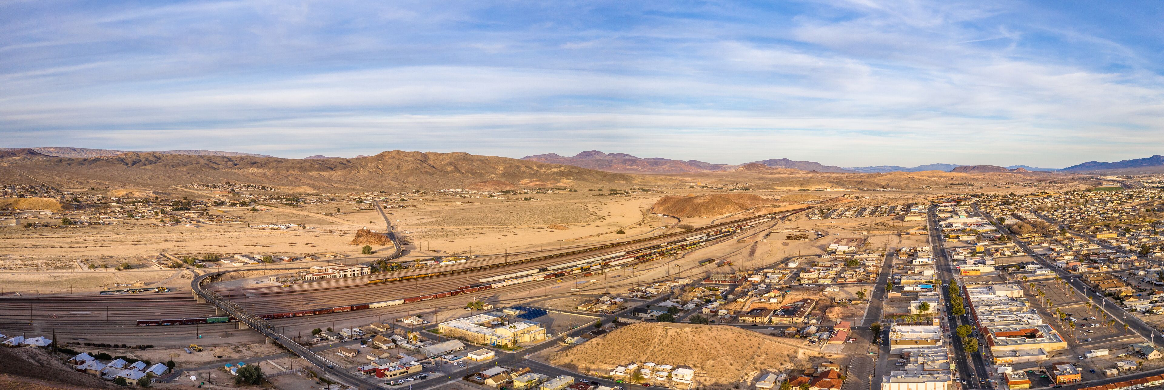A desert town with a train yard and mountains in the background.