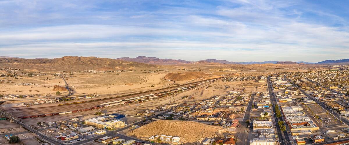 A desert town with a train yard and mountains in the background.