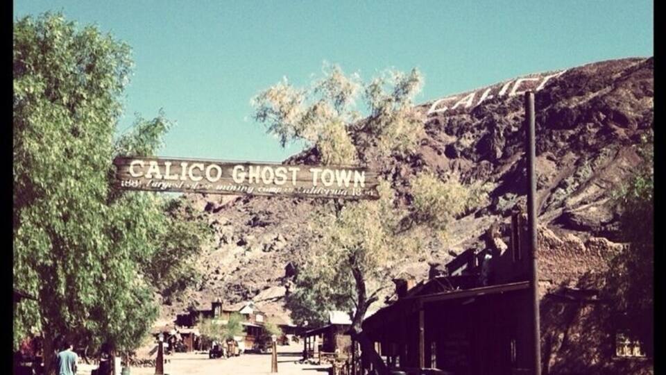 A sign reading "CALICO GHOST TOWN" with a desert landscape and buildings in the background.