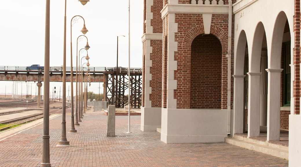 A brick building with arches and a tower, street lamps, and a bridge in the background.