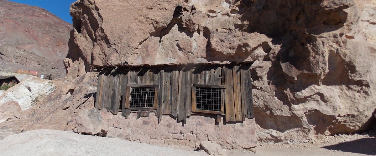 A rustic stone structure with wooden walls and two barred windows.