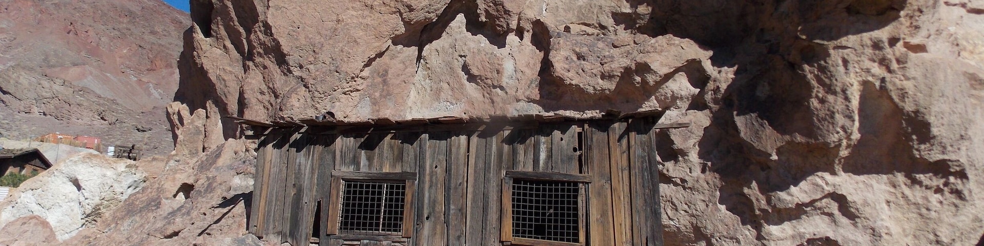A rustic stone structure with wooden walls and two barred windows.