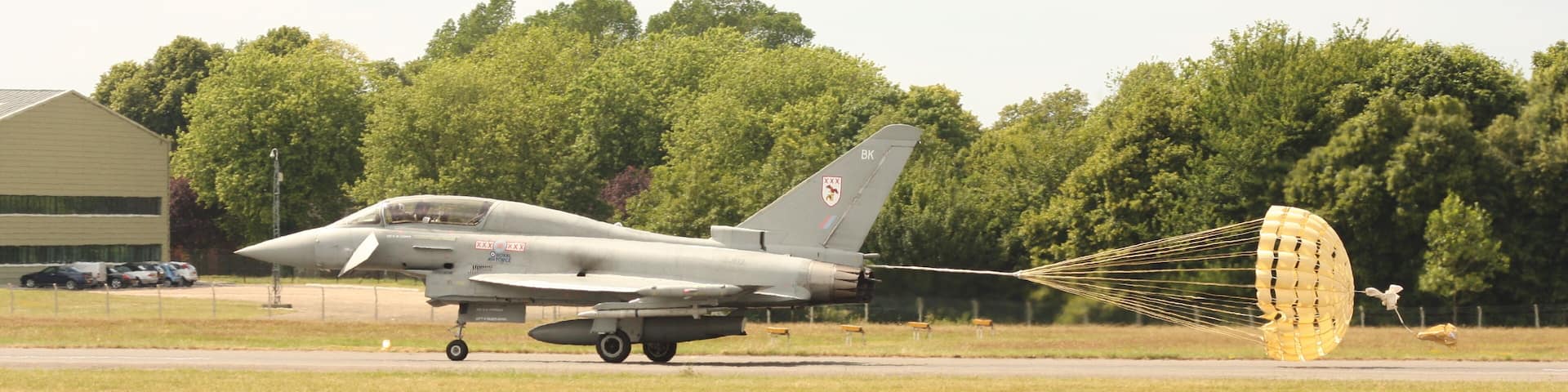 A military aircraft on a runway with a parachute deployed.