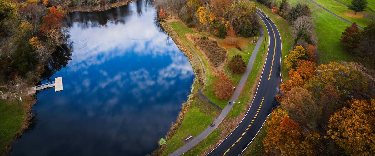 A winding road alongside a lake with autumn-colored trees.