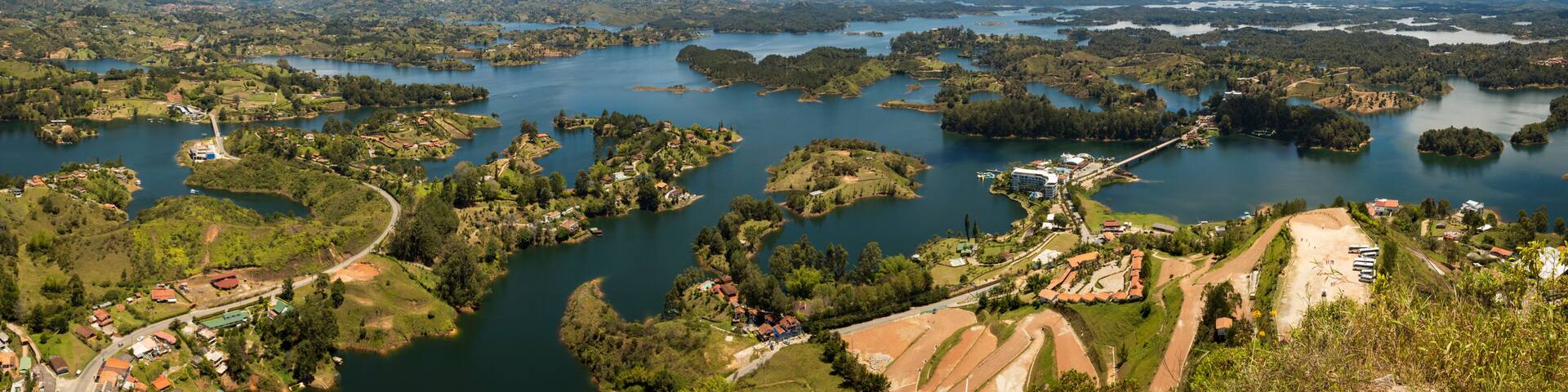 A panoramic view of a lake surrounded by lush greenery and scattered buildings.