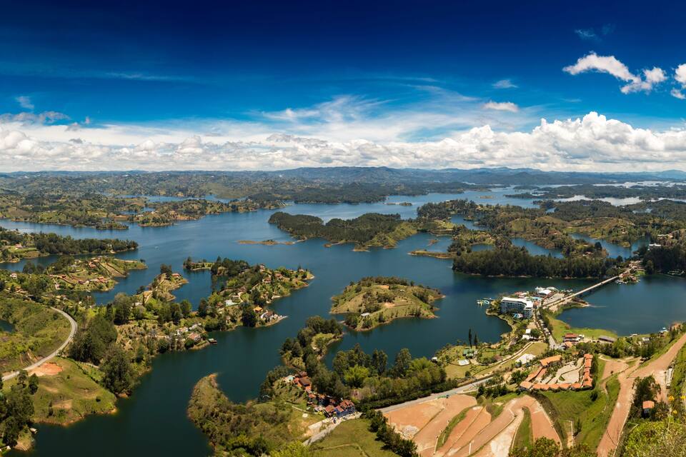 A panoramic view of a lake surrounded by lush greenery and scattered buildings.