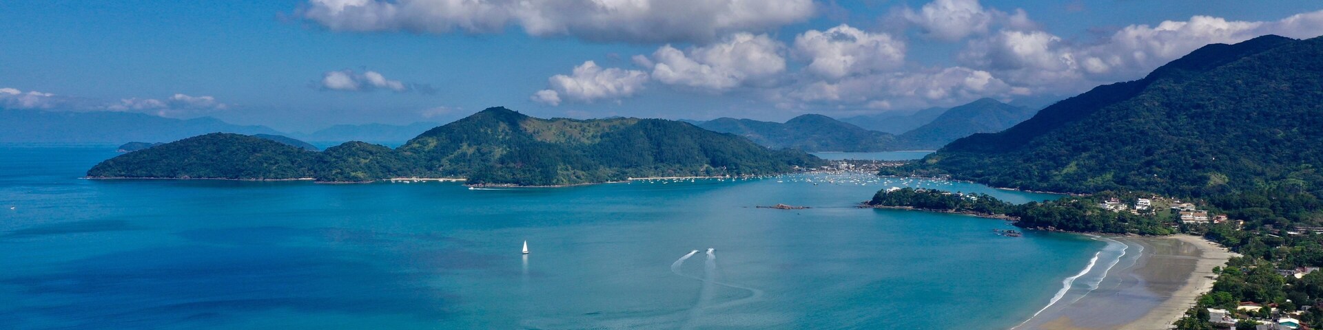 Paisagem costeira com águas turquesa cristalinas, uma praia arenosa e colinas verdejantes ao fundo.
