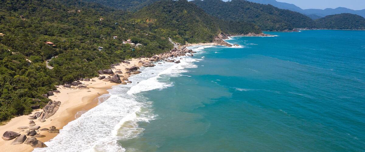 A coastal landscape with a sandy beach, turquoise waters, and a forested hillside.