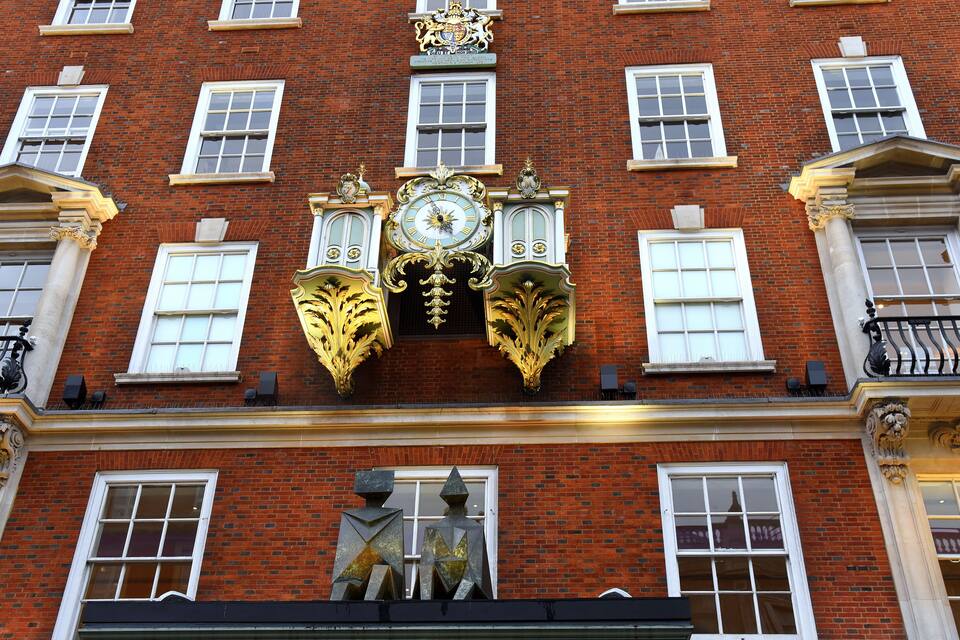Un edificio de ladrillo rojo con detalles ornamentales dorados, que incluyen un reloj y paneles decorativos.