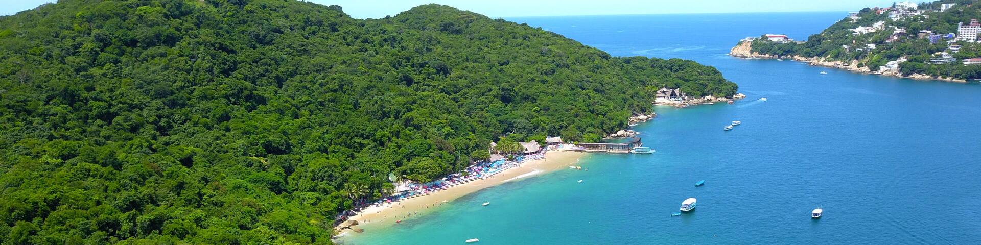 A coastal landscape with a beach, boats, and lush greenery.