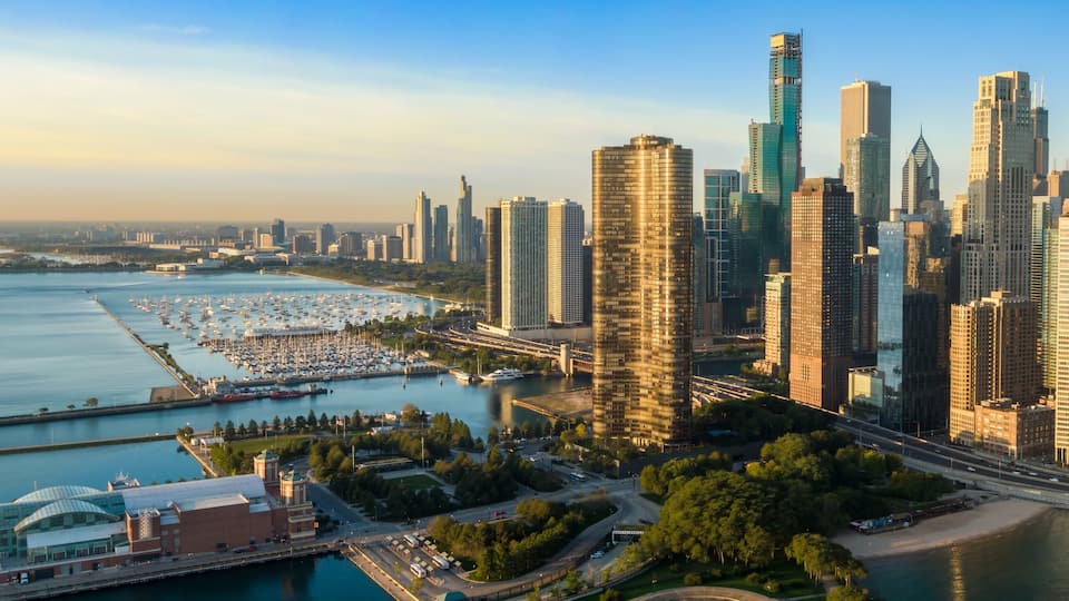 A city skyline with modern skyscrapers, a marina with boats, and a coastal park.