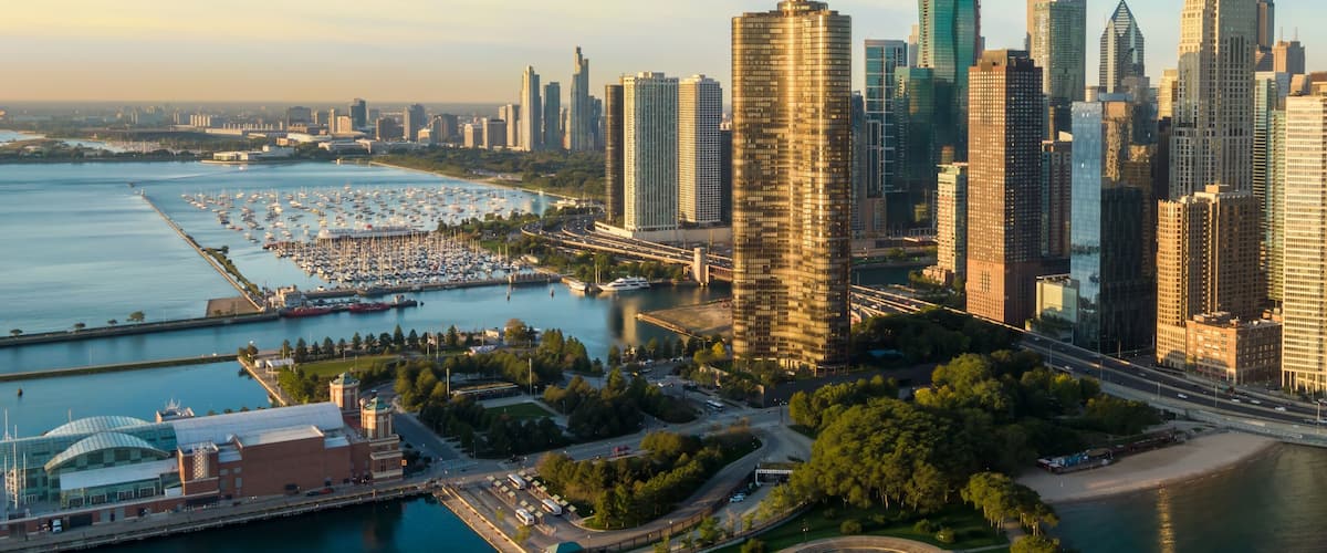 A city skyline with modern skyscrapers, a marina with boats, and a coastal park.
