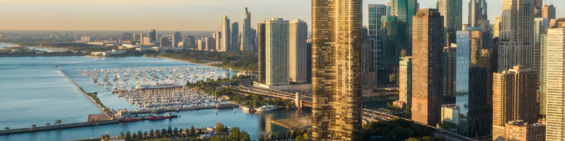 A city skyline with modern skyscrapers, a marina with boats, and a coastal park.