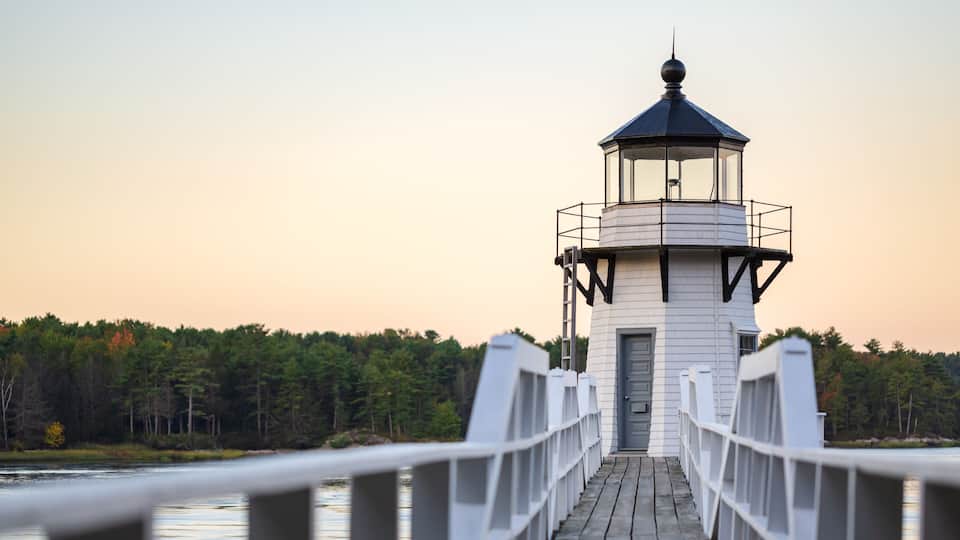 A lighthouse on a wooden pier with a forested shoreline in the background.