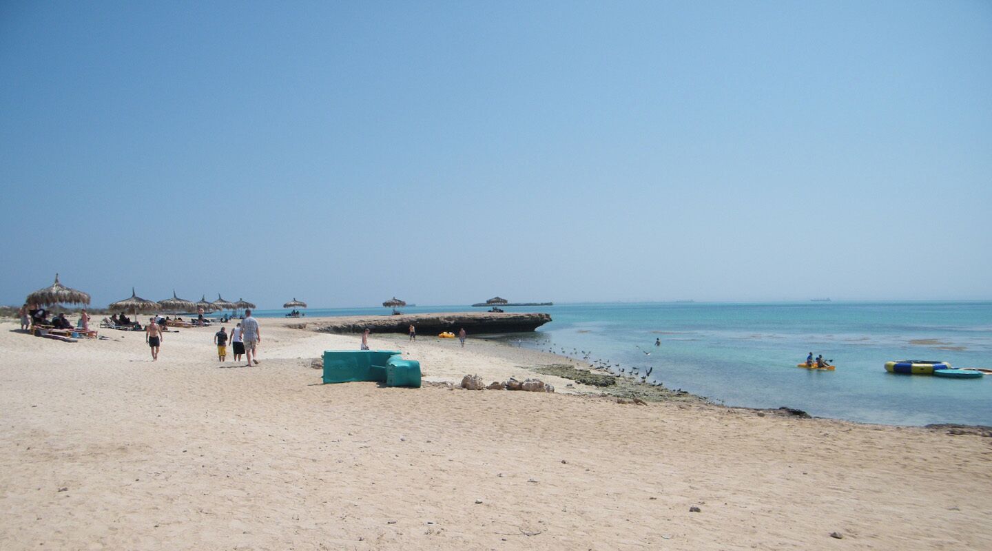 A sandy beach with thatched umbrellas, a rocky outcrop, and calm waters.